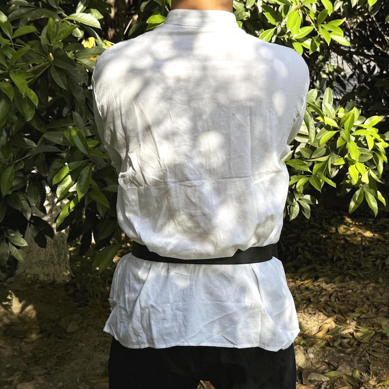 May include: A white long-sleeved shirt with a black belt. The shirt has a mandarin collar and is made of a lightweight fabric.