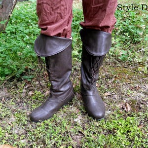 May include: Brown leather knee-high boots with a lace-up design and a folded-over cuff. The boots are worn with burgundy-coloured trousers. The boots are designed in the style of historical footwear.