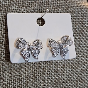May include: A pair of silver bow-shaped earrings with clear crystal accents.