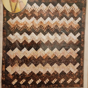 May include: A quilt pattern titled "Zig A Zag Quilt" by Eleanor Burns. The pattern features a repeating zig-zag design in shades of brown and beige. The "Quilt in a Day" company logo is visible.