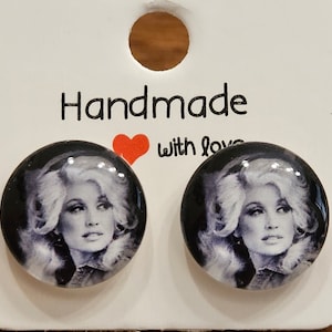 May include: A pair of black and white round stud earrings featuring a photo of a woman with blonde hair. The earrings are handmade with love.