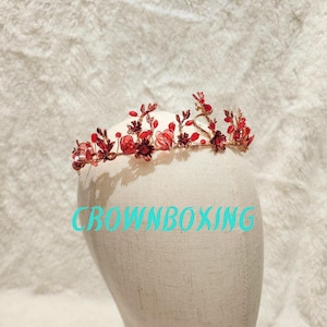 May include: A gold crown with red and pink floral accents. The crown is made of metal and has a delicate design.