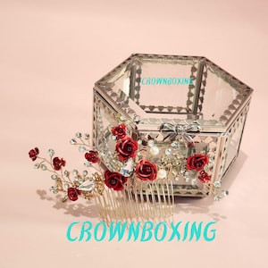 May include: A gold-toned hair comb adorned with red roses, crystals, and pearls. The comb is next to a mirrored, hexagonal jewelry box. The text "CROWNBOXING" is visible on the image.