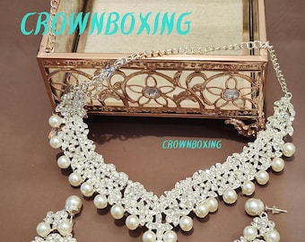 May include: A silver-toned necklace and earring set with faux pearls and clear rhinestones. The necklace has a floral design with dangling pearls. The earrings are a smaller version of the necklace. The text "CROWNBOXING" is visible in the image.