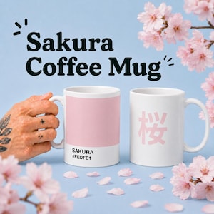 May include: Two white ceramic coffee mugs. One mug features a pink color block with the word "Sakura" and the color code #FEDFE1. The other mug has the Japanese character for cherry blossom in pink.