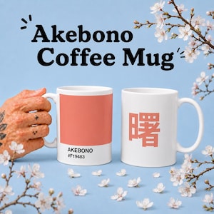 Op de afbeelding: Twee witte keramische koffiemokken. Eén mok heeft een koraalkleurig blok met de tekst "AKEBONO #F19483". De andere mok heeft een koraalkleurig Japans karakter. Boven de mokken staat "Akebono Coffee Mug".