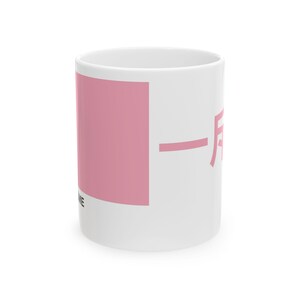 May include: White ceramic mug with a pink rectangular design and Japanese characters. The mug also has the word "ME" printed on it. The mug is a standard size for coffee or tea.