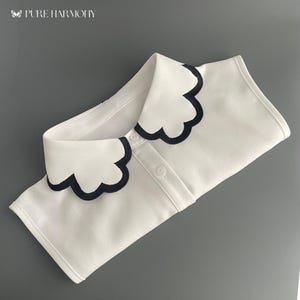 Könnte beinhalten: Weißes Hemd mit Kragen und schwarzem, gewelltem Besatz am Kragen.