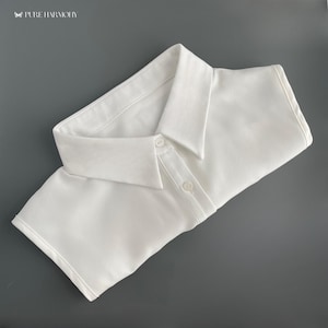 Puede incluir: Un cuello de camisa blanco, desmontable, con un diseño clásico en punta. El cuello tiene dos botones y está hecho de una tela suave y crujiente. La esquina superior izquierda de la imagen tiene el texto "PURE HARMONY".