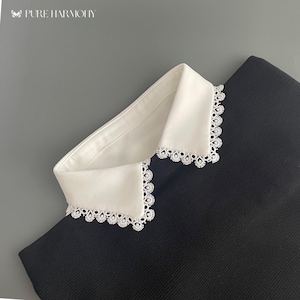May include: A black collared shirt with a white lace trim collar. The collar is folded over and the lace trim is visible.