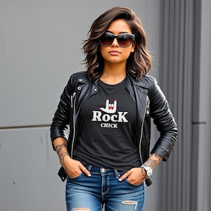 May include: A woman wearing a black leather jacket over a black t-shirt with a white graphic that says "Rock Chick" and a hand gesture. She is wearing blue jeans and sunglasses.
