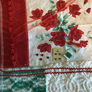 May include: A collection of craft supplies including a red textured fabric strip with pom-pom trim, a white fabric piece with a red rose floral print, a white lace ribbon, four small red buttons, a card of green buttons, and green thread.
