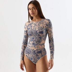 May include: A long-sleeved bodysuit and high-waisted bottoms featuring a floral pattern in navy blue on a nude background. The bodysuit has a crew neck and the bottoms have a high waist. The floral design is detailed and covers the entire garment.