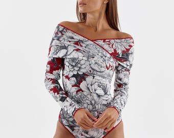 Op de afbeelding: Een bodysuit met lange mouwen en een bloemenpatroon in wit, grijs en zwart op een rode achtergrond. De bodysuit heeft een off-shoulder ontwerp en rode randen.