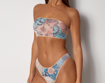 May include: A two-piece swimsuit set featuring a bandeau top and high-cut bottoms. The set is patterned with a patchwork design in shades of blue, pink, and beige, with floral and paisley motifs. The edges are trimmed with a light beige.