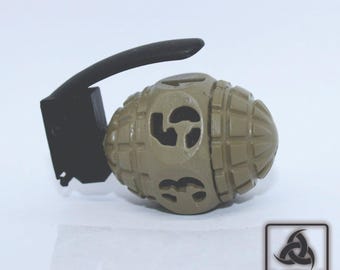 May include: A tan-colored replica grenade with a black handle. The grenade has a textured surface and a design of a five-pointed star on each side.