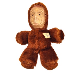 May include: A brown plush monkey toy with a human-like face. The toy has a tag that says "Gunne  -  Co. Ltd."
