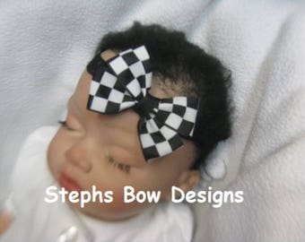 Könnte beinhalten: Ein Baby trägt ein schwarz-weiß kariertes Schleifenband. Das Band ist oben auf dem Kopf des Babys zu einer Schleife gebunden. Das Baby trägt einen weißen Strampler. Der Text "Stephs Bow Designs" ist im Bild sichtbar.