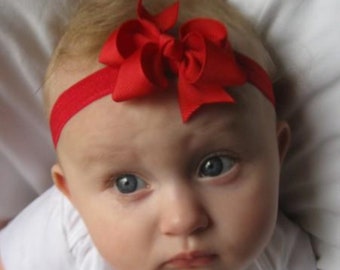 Può includere: Un bambino che indossa una fascia rossa con un grande fiocco rosso. La fascia è realizzata in un materiale morbido ed elastico e il fiocco è realizzato in nastro di grosgrain.