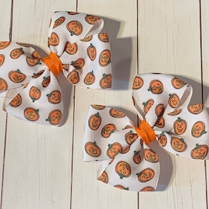 May include: Two white hair bows with orange centres and a pumpkin pattern.
