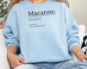 May include: A light blue sweatshirt with the text "Macaron: (noun) French for 'One Bite Won't Hurt.'" printed on the front.