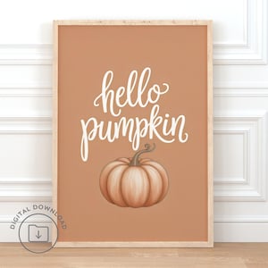 Könnte beinhalten: Ein gerahmter Kunstdruck mit hellbraunem Hintergrund und den Worten "hello pumpkin" in weißer Schrift. Unter dem Text befindet sich eine detaillierte Illustration eines Kürbisses. Der Rahmen ist hellbraun.