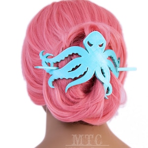 May include: A light blue octopus hair clip with a wooden stick. The clip is in the shape of an octopus with tentacles and is being worn in a pink wig.