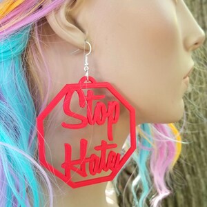 May include: Red octagon-shaped earrings with the words "Stop Hate" written in white lettering.