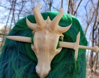 May include: A beige, 3D printed hair clip shaped like a skull with horns, pierced by a wooden sword.