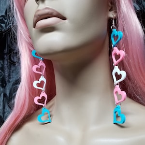 May include: A pair of long dangle earrings with a chain of hearts. The hearts are in shades of pink, white, and blue.