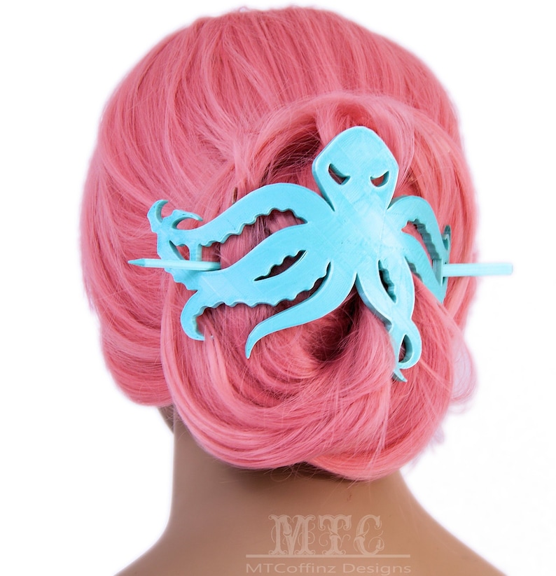May include: A light blue octopus hair clip with a wooden stick. The clip is in the shape of an octopus with tentacles and is being worn in a pink wig.