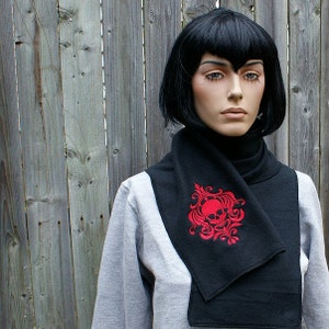 May include: Black scarf with a red embroidered skull and floral design. The scarf is folded and worn around the neck.