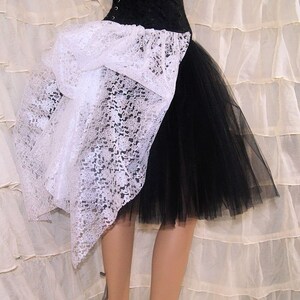 Pu&ograve; includere: Una gonna di tulle nero con un'sovrapposizione di pizzo bianco. La sovrapposizione di pizzo &egrave; raccolta nella parte anteriore e cade lateralmente.