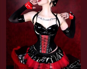 May include: A black and red corset with a red lace-up front and a black skirt with a red tulle overlay. The corset has a shiny, patent leather finish. The model is wearing black gloves and has a tattoo on her chest that reads "Live the Dreamers of Dreams".