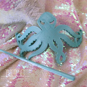 May include: A teal blue octopus hair comb with a stick. The comb is made of plastic and has a detailed design. The stick is also teal blue and is made of plastic.