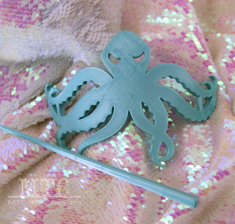 May include: A teal blue octopus hair comb with a stick. The comb is made of plastic and has a detailed design. The stick is also teal blue and is made of plastic.