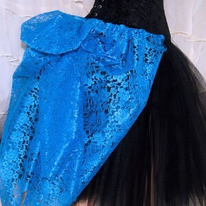 May include: A black tulle skirt with a large blue lace bow on the side. The lace is a delicate floral pattern.