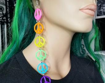 May include: Rainbow peace sign earrings with a silver chain. The earrings are long and dangle from the earlobe.