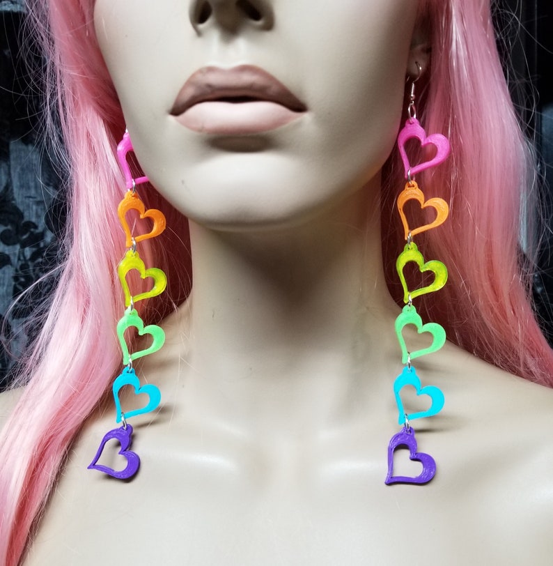 May include: Rainbow heart dangle earrings with a silver hook. The hearts are in the order of red, orange, yellow, green, blue, and purple.