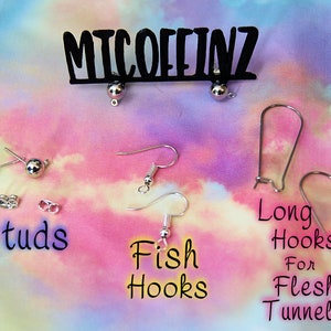 May include: A variety of earring findings, including studs, fish hooks, and long hooks for flesh tunnels. The findings are silver in color and are displayed on a pink and blue tie-dye background. The text "MICOFFINZ" is displayed at the top of the image.