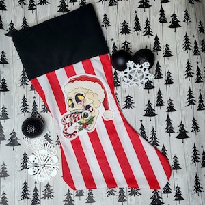 May include: A red and white striped Christmas stocking with a black cuff. The stocking features a skull with candy canes and a holly sprig.