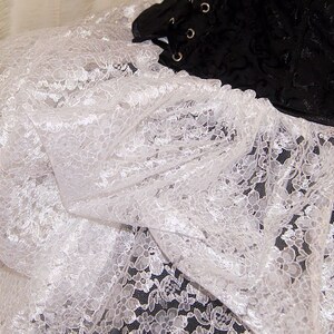 Pu&ograve; includere: Tessuto di pizzo bianco con un delicato motivo floreale. Il pizzo &egrave; morbido e fluido, con una texture leggermente trasparente.