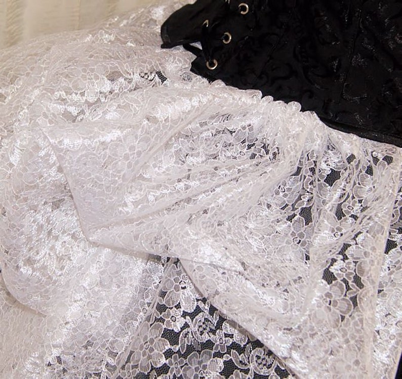 Pu&ograve; includere: Tessuto di pizzo bianco con un delicato motivo floreale. Il pizzo &egrave; morbido e fluido, con una texture leggermente trasparente.
