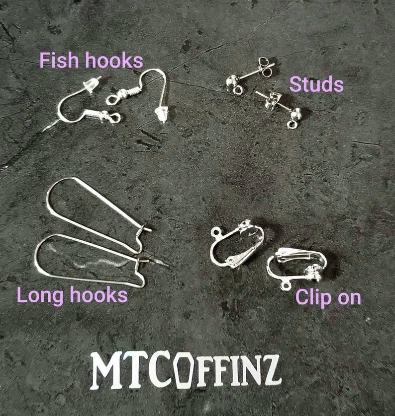 K&ouml;nnte beinhalten: Eine Auswahl an Ohrring-Verschl&uuml;ssen, darunter Fischhaken, Ohrstecker, lange Haken und Clip-Ohrringe. Die Verschl&uuml;sse sind silberfarben und werden auf einer grauen, strukturierten Oberfl&auml;che pr&auml;sentiert.