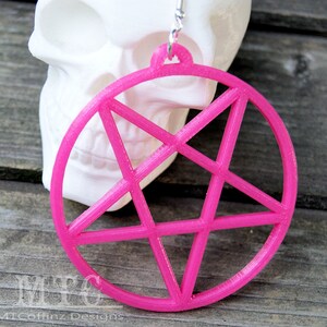 May include: A pair of pink, large, circular earrings with a pentagram design. The earrings are made of plastic and have a shiny finish.
