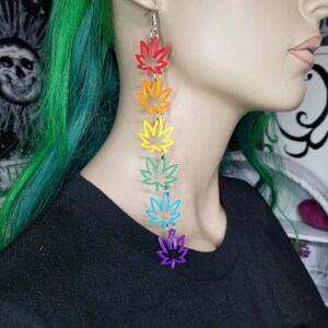 May include: Rainbow colored marijuana leaf dangle earrings. Each leaf is a different color of the rainbow, starting with red and ending with purple.