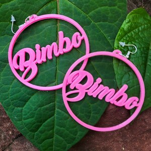 May include: A pair of pink hoop earrings with the word "Bimbo" written in a cursive font on each earring.