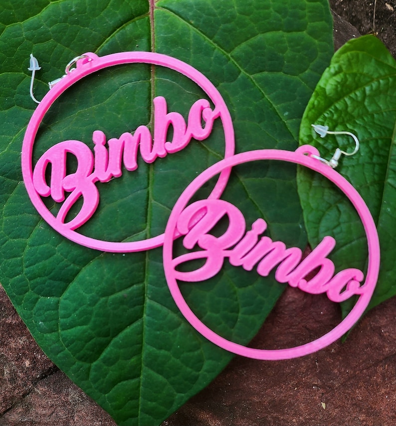 May include: A pair of pink hoop earrings with the word "Bimbo" written in a cursive font on each earring.