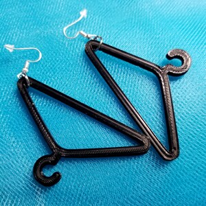 May include: A pair of black hanger-shaped earrings with silver hooks. The earrings are made of a 3D printed material.