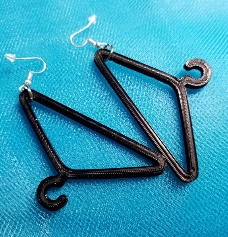 May include: A pair of black hanger-shaped earrings with silver hooks. The earrings are made of a 3D printed material.